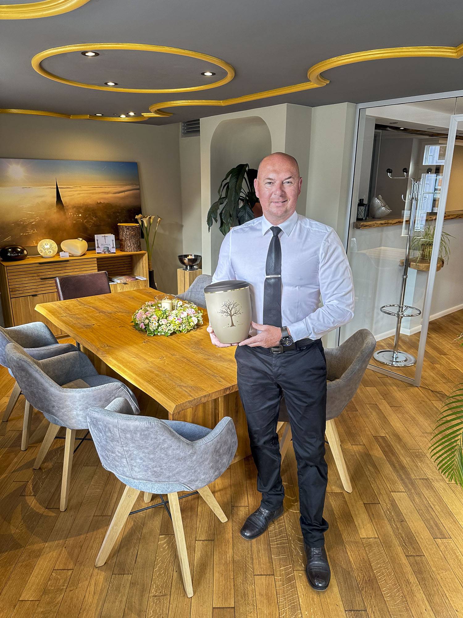 Geschäftsinhaber Alexander Mehl vom Bestattungshaus Mehl in der Schweriner Altstadt steht im modernen Besprechungsraum des denkmalgeschützten Hauses Alte Münze in der Münzstraße und hält eine Urne.